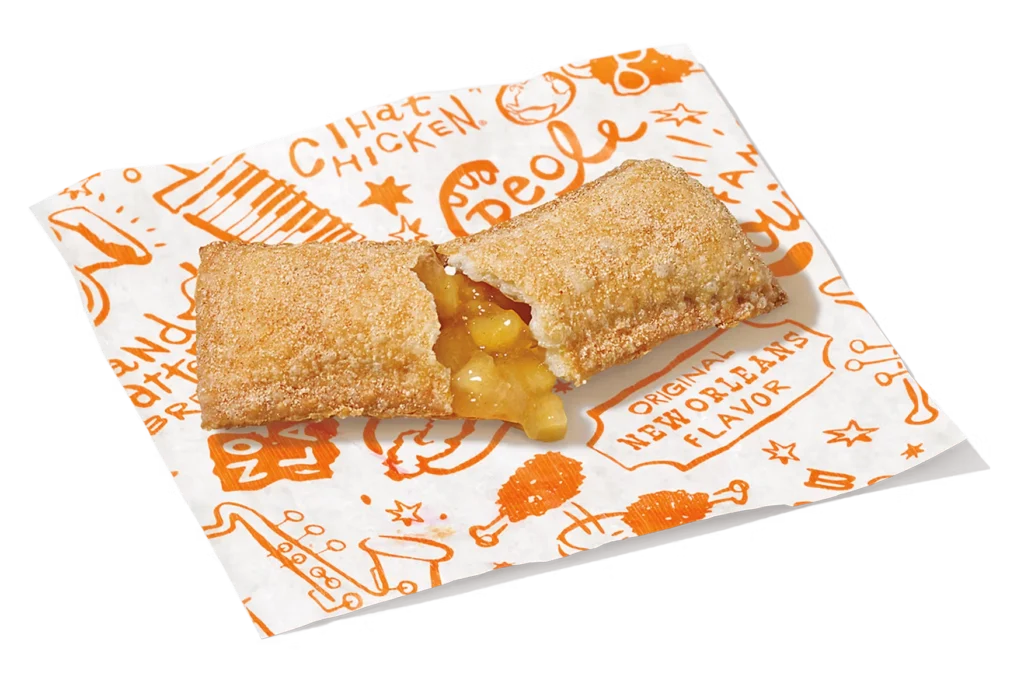 "Cinnamon Apple Pie with a bite taken out, showing apple filling, on a paper napkin with a branded design."