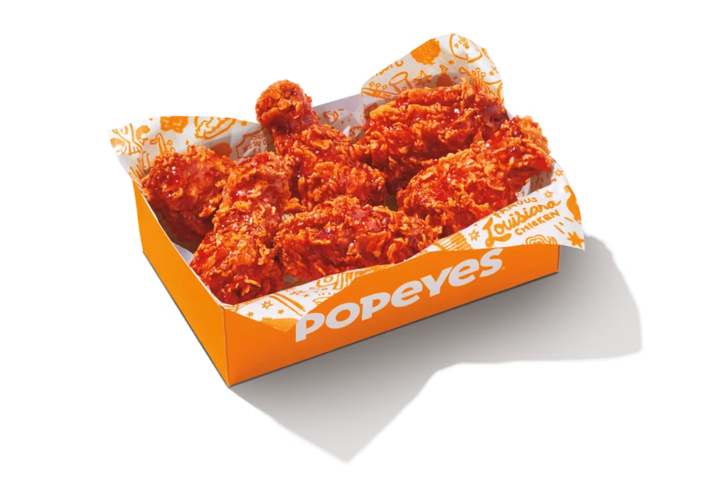 "Spicy Bone-In Wings in Popeyes branded packaging, coated in a vibrant red spicy seasoning."