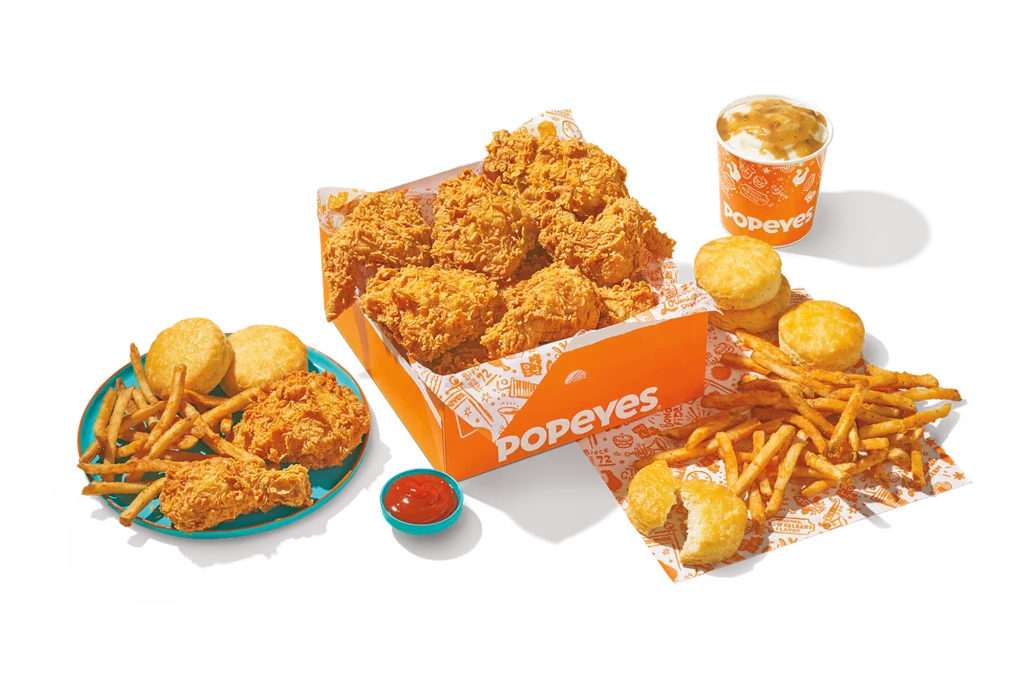 12Pc Chicken Family Meal with crispy fried chicken, fries, biscuits, dipping sauce, and a drink in Popeyes packaging."