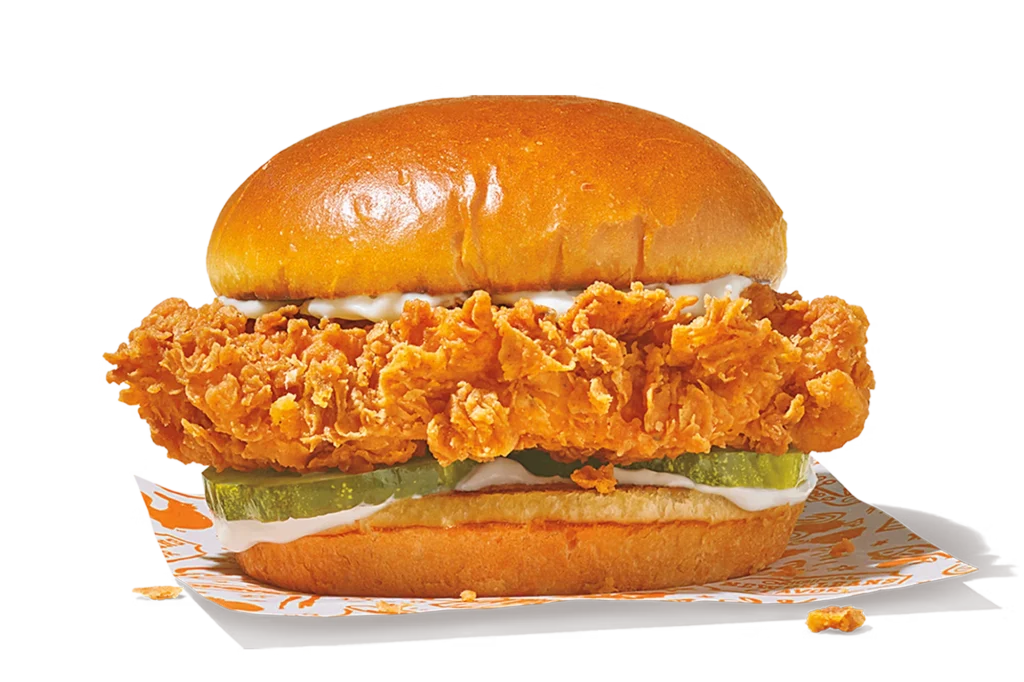 "Chicken Sandwich with fried chicken, pickles, and mayonnaise in a bun."