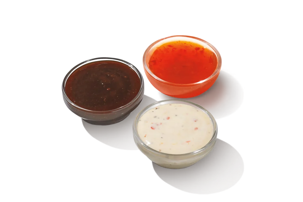 "Three bowls of wing flavor sauces: one with a brown sauce, one with a red sauce, and one with a white sauce, on a white background."