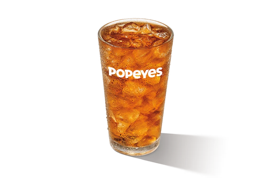 "Glass of iced tea with ice cubes, Popeyes logo on the glass, on a white background."